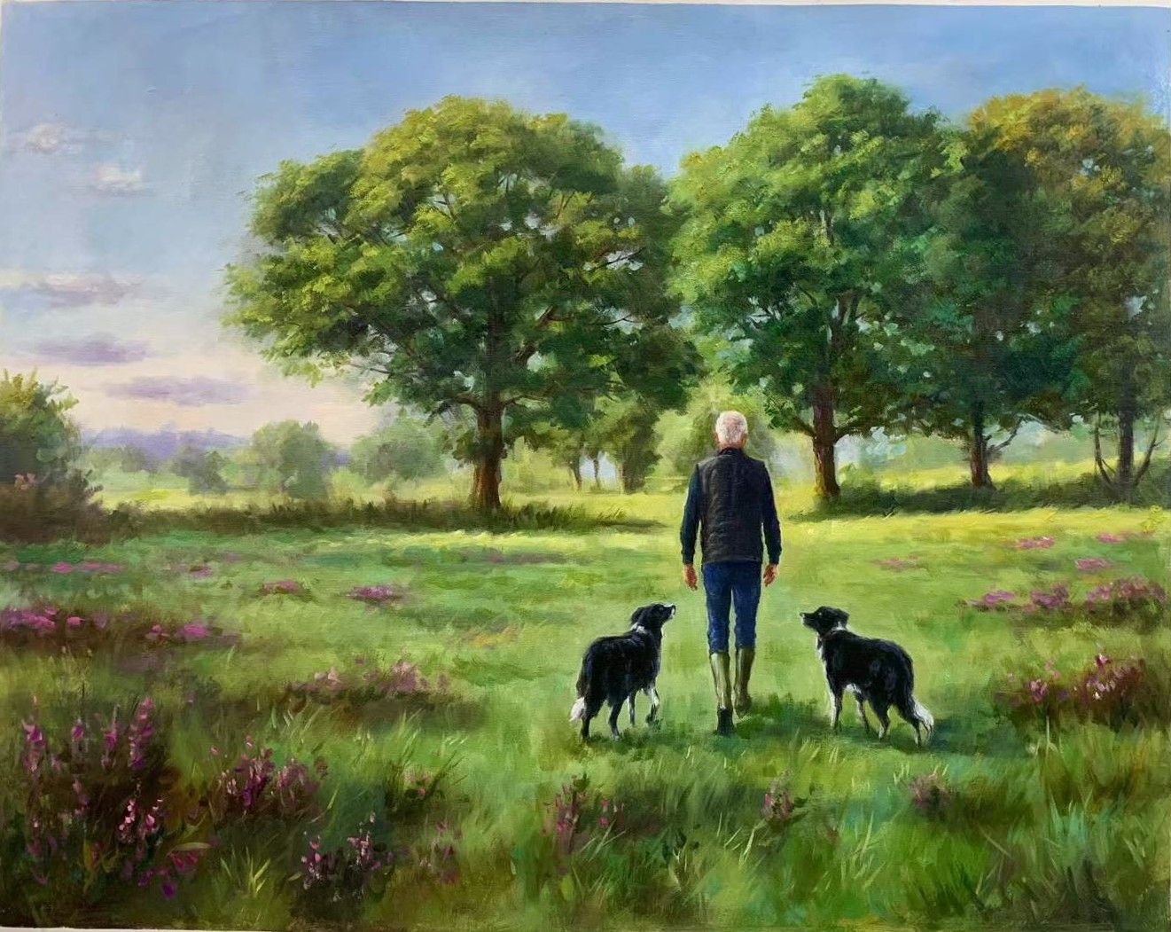 A man walking with two black and white dogs through sunlit grass.