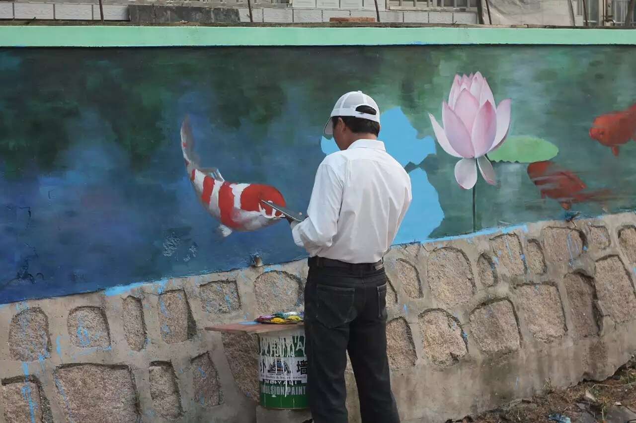 A painter at work on a hand-painted koi and lotus wall mural