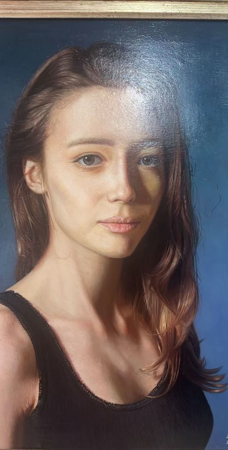 A young woman with long brown hair and a black top beneath a visible ornate frame edge.