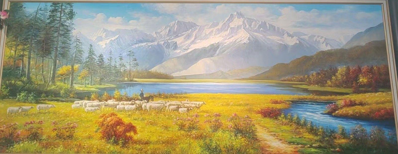 A flock of sheep grazes beside a mountain lake beneath bright peaks and autumn-colored hills.